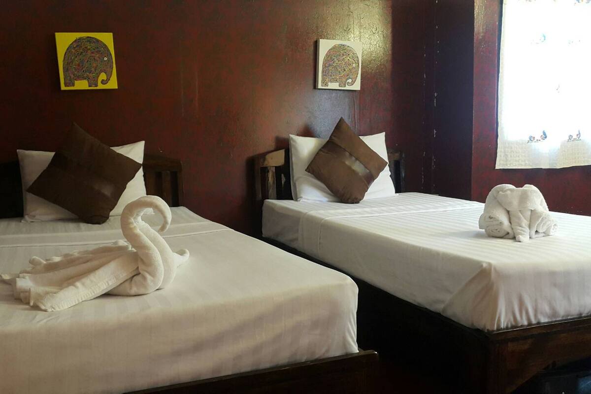 Two beds with white linens, brown pillows, and a swan-shaped towel on the left bed.