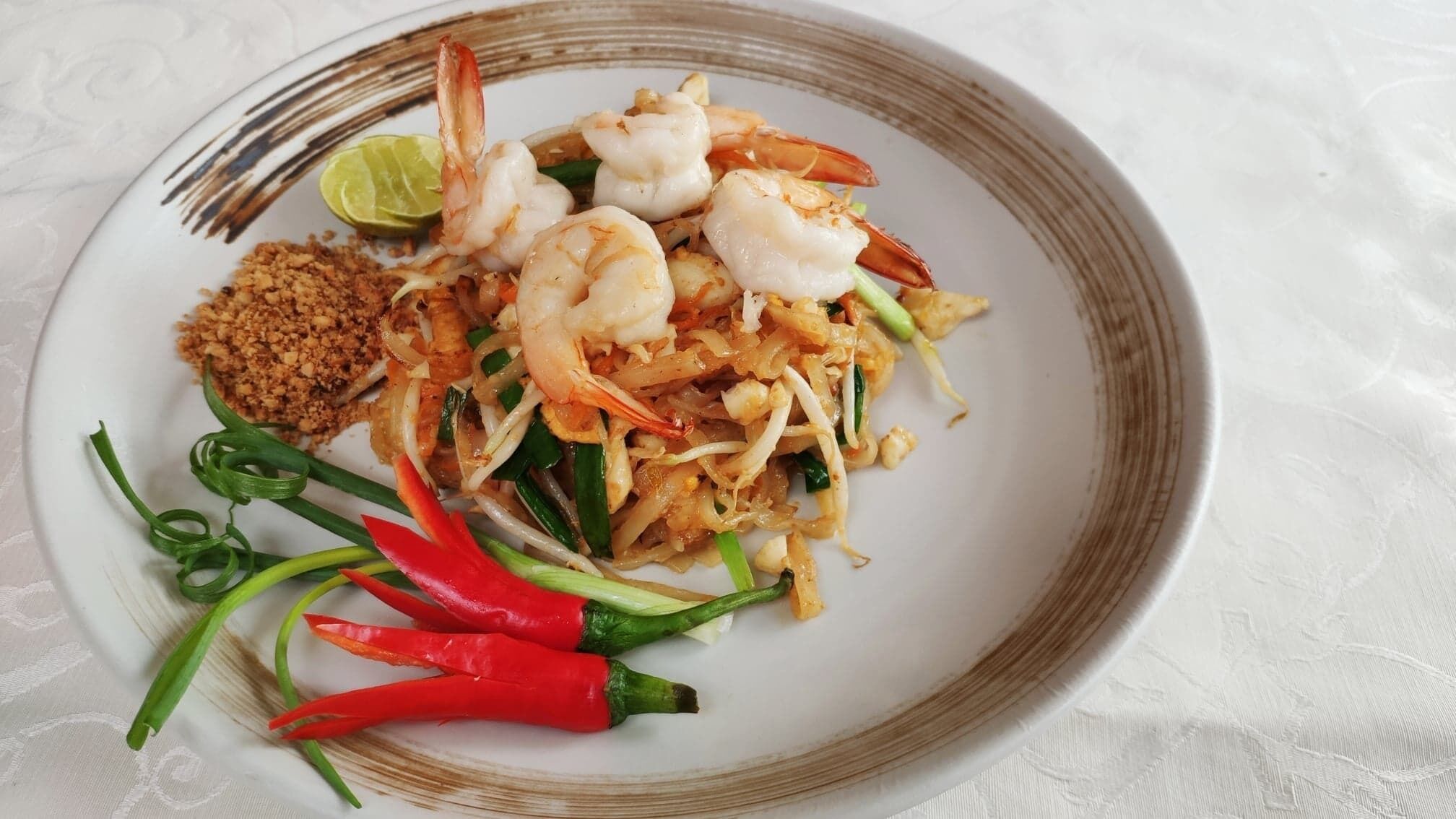 A plate of Pad Thai with shrimp, lime, and red chili peppers.