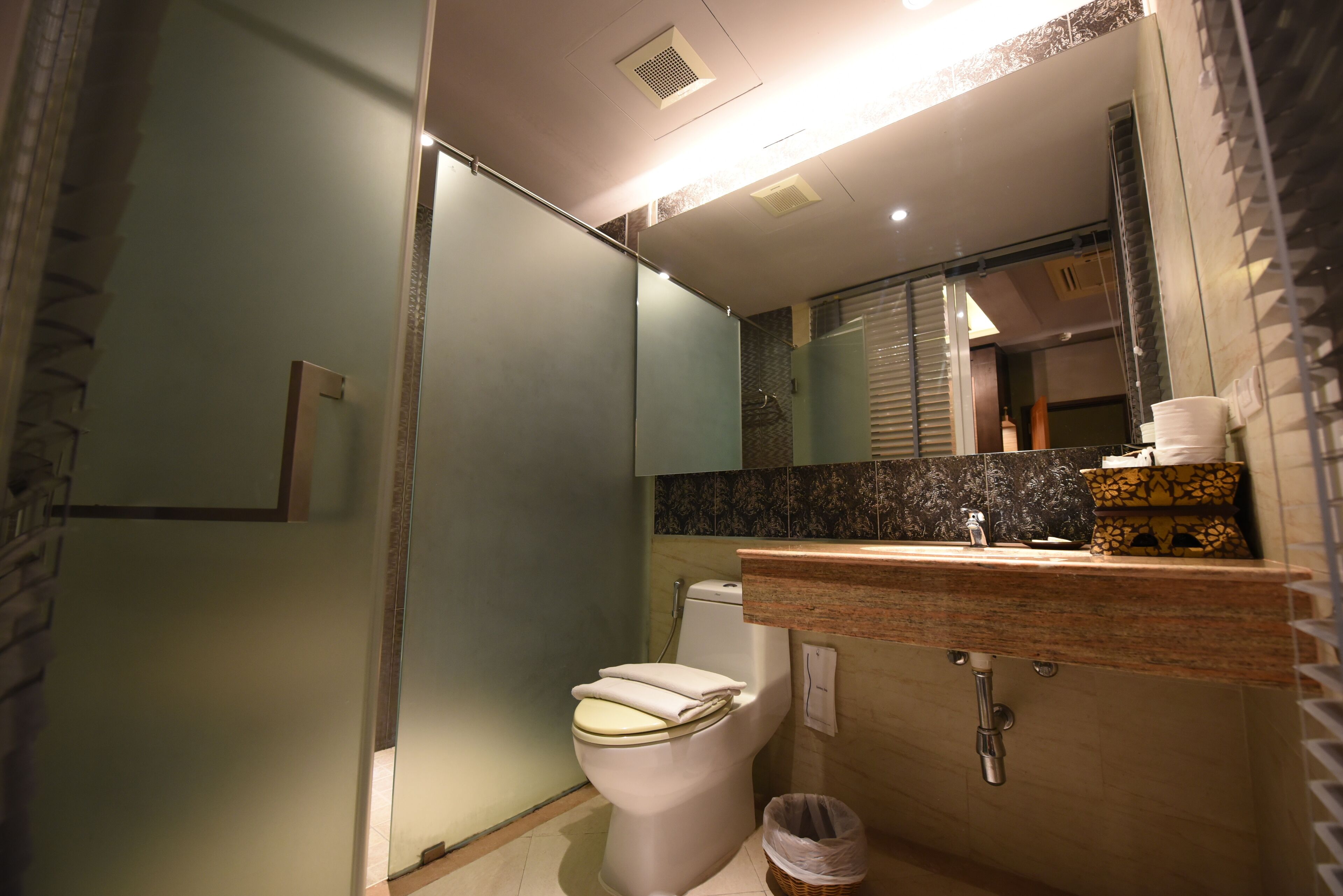A modern bathroom with a glass shower enclosure, a white toilet, a sink with a marble countertop, and a mirror above the sink.