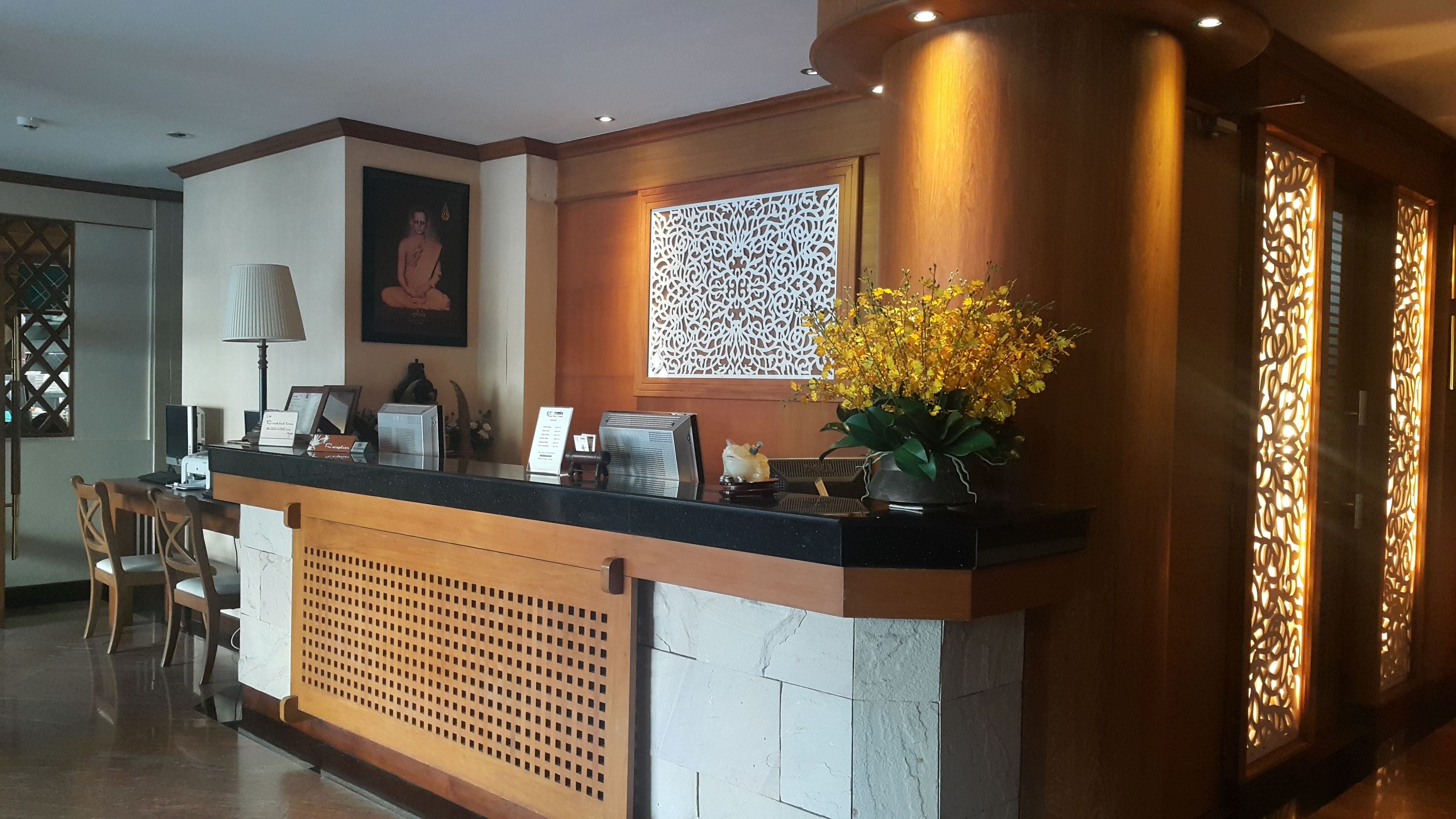 Un comptoir d’accueil avec un ordinateur, un téléphone et un vase rempli de fleurs jaunes.