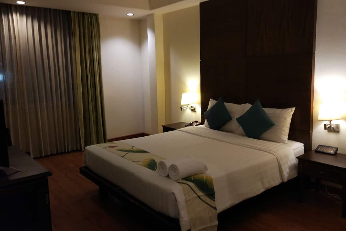 A hotel room with a large bed, a desk, a chair, a lamp, and a curtain.