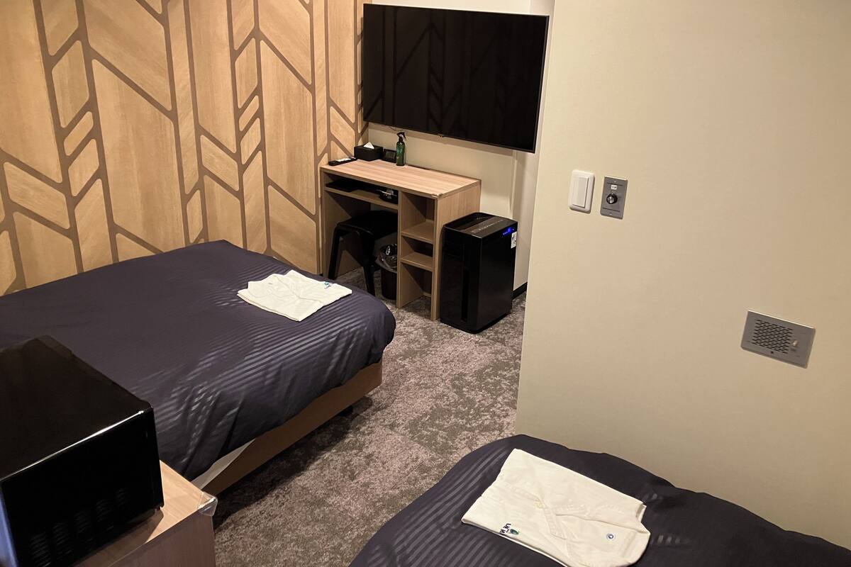 A hotel room with a bed, a desk, a computer, and a TV.