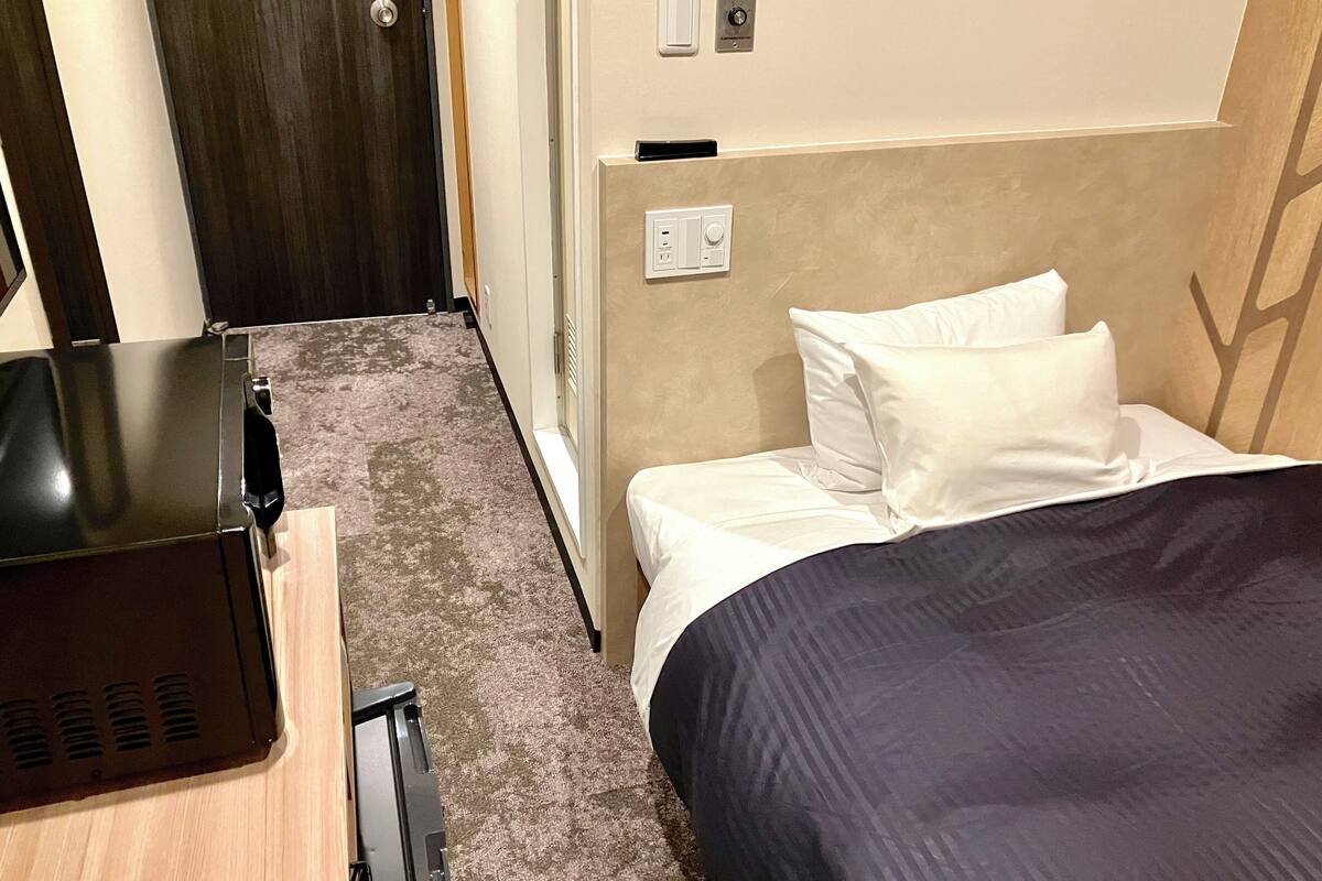 A hotel room with a bed, a desk, and a door.