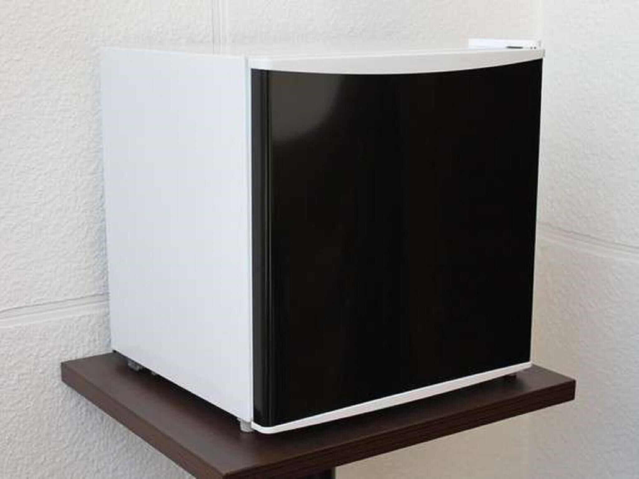 A white and black refrigerator on a wooden shelf against a textured wall.