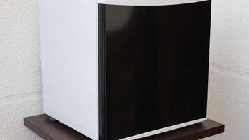 A white and black refrigerator on a wooden shelf against a textured wall.