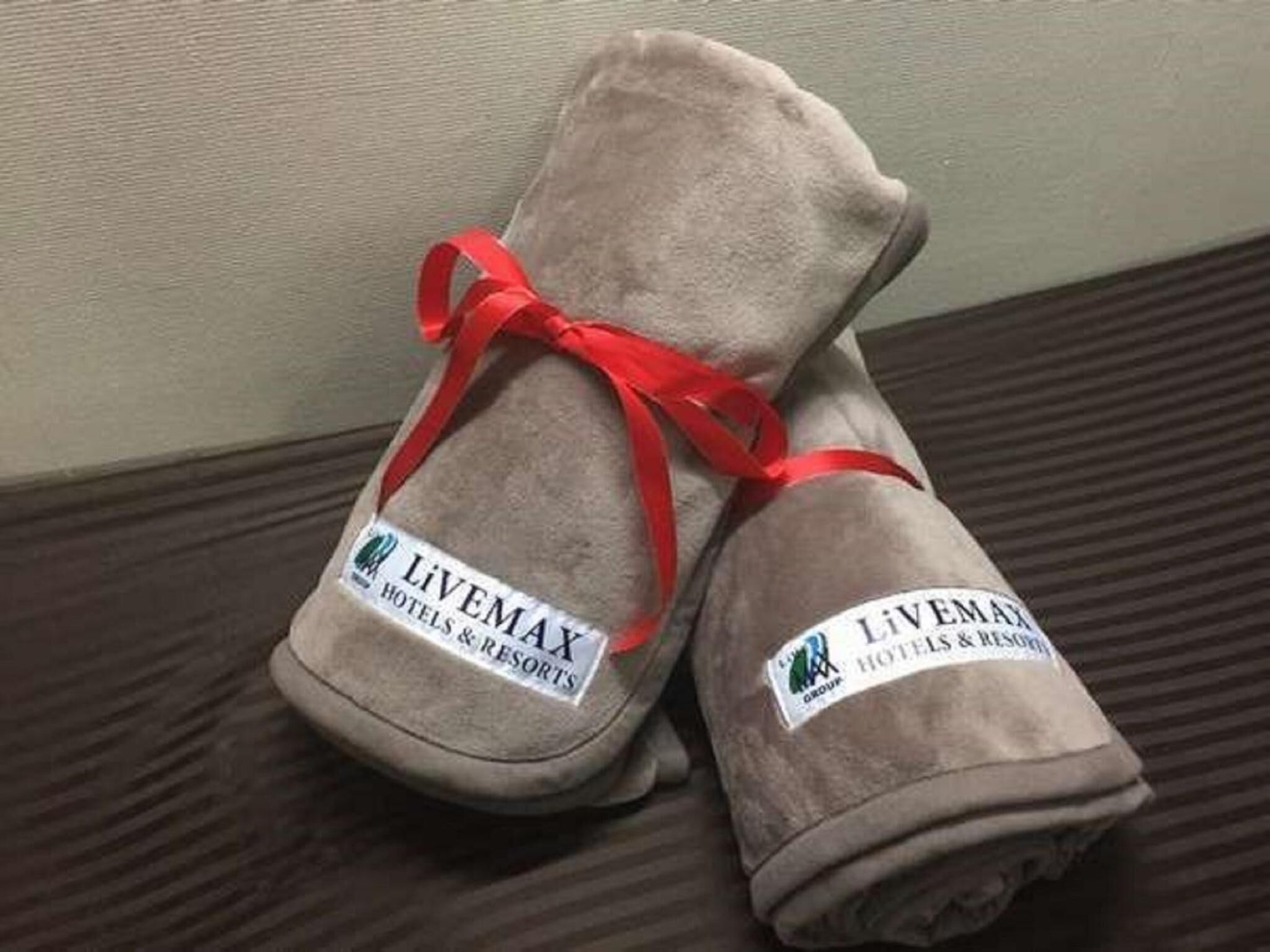 Dos toallas enrolladas con una cinta roja atada, con el nombre 'LIVEMAX HOTELS & RESORTS'.