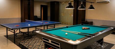 A pool table with a billiard cue, a ping pong table, and a pool table with balls and cues.