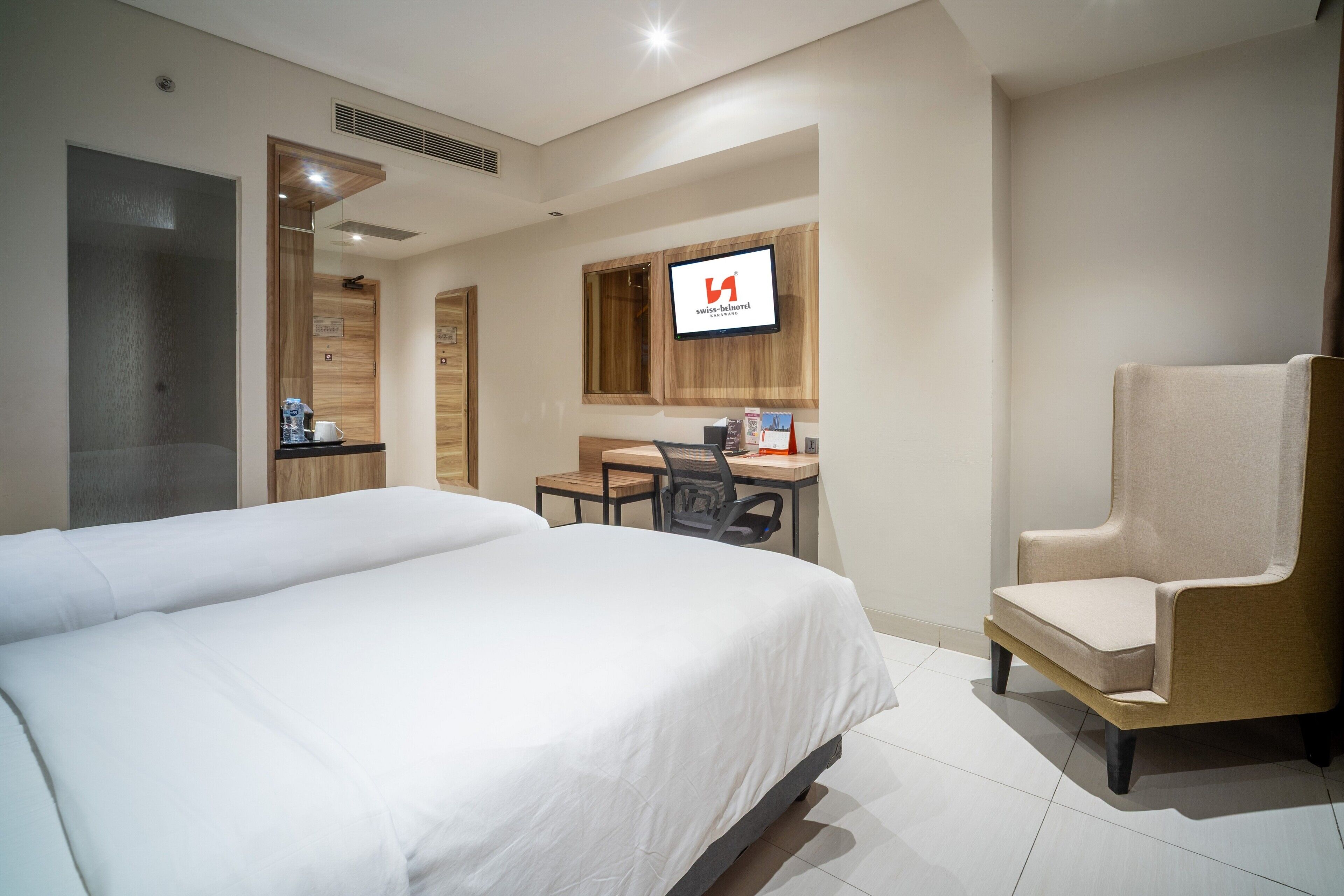 A hotel room with two beds, a desk, a chair, and a television on the wall.
