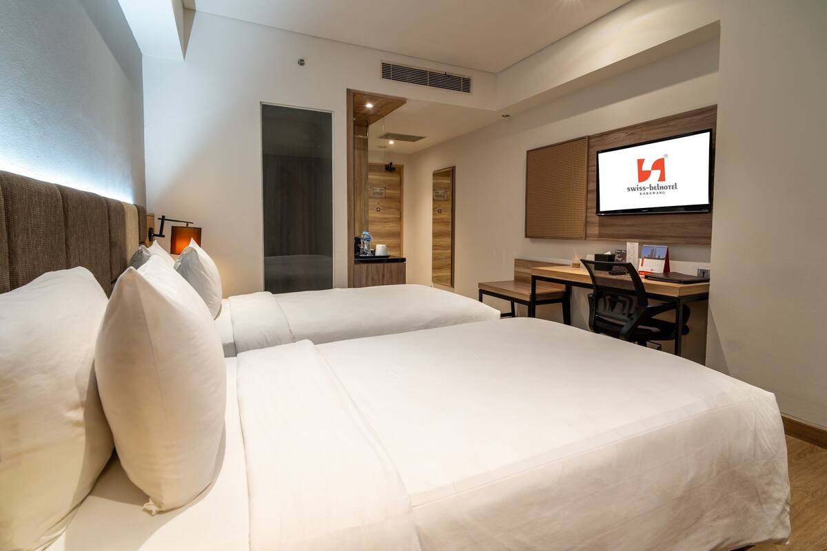 Habitación de hotel con dos camas, un escritorio, una silla, un televisor y un panel de pared de madera.