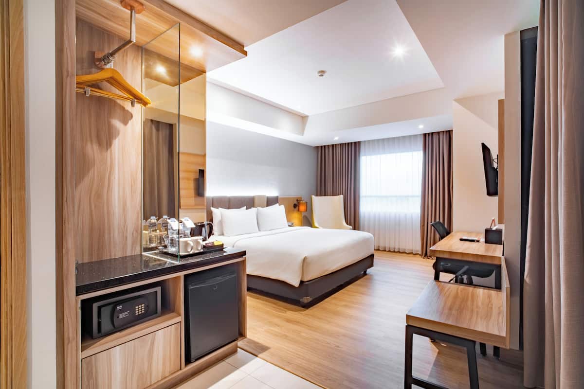 Una habitación de hotel moderna con cama, mesita de noche, escritorio y televisión integrada.