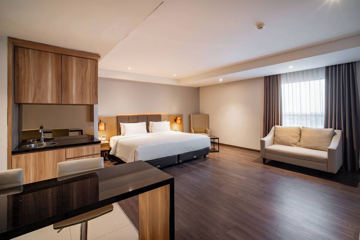 Una habitación de hotel moderna con cama, sofá, zona de comedor y kitchenette.