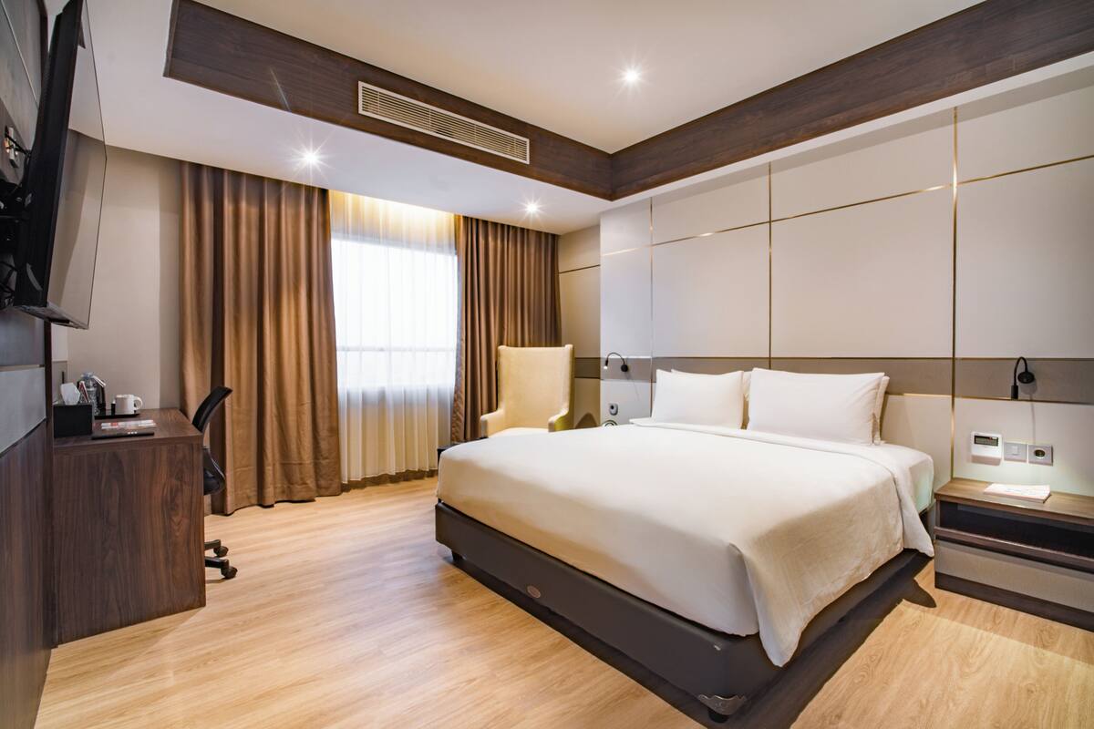 Una habitación de hotel moderna con una cama grande, suelo de madera, un escritorio con silla y televisión.