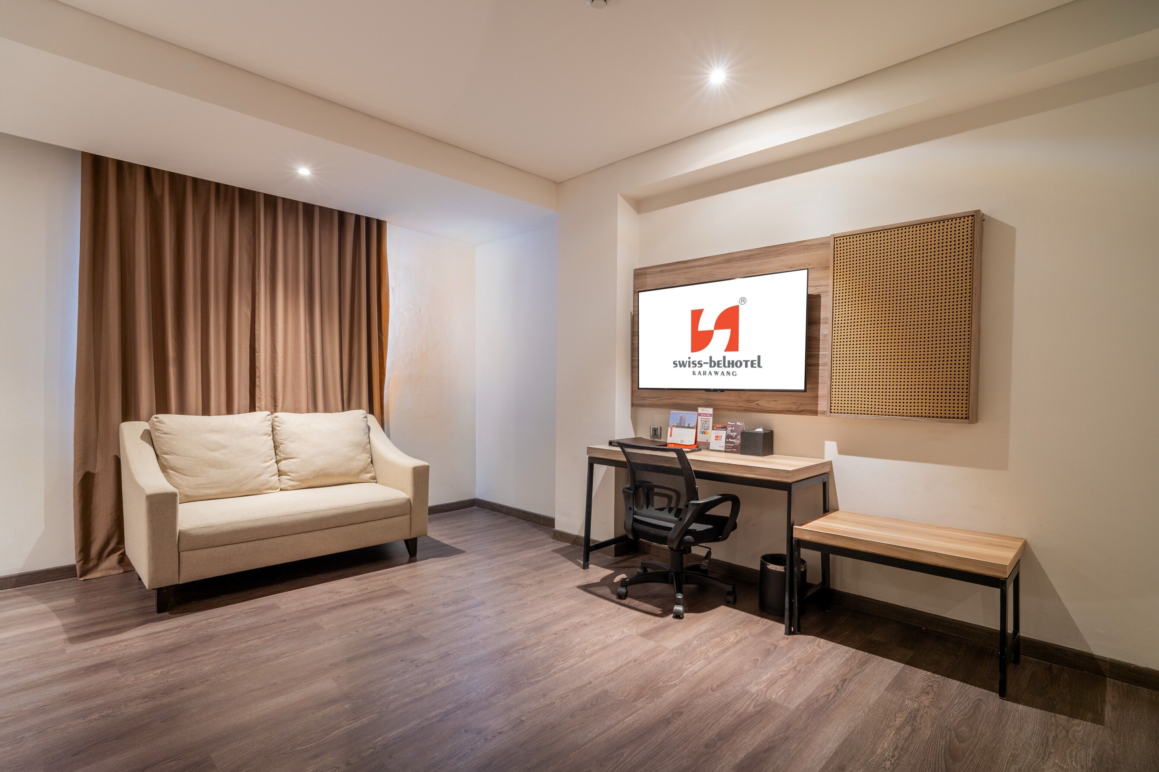 A hotel room with a sofa, desk, chair, and a wall-mounted sign.