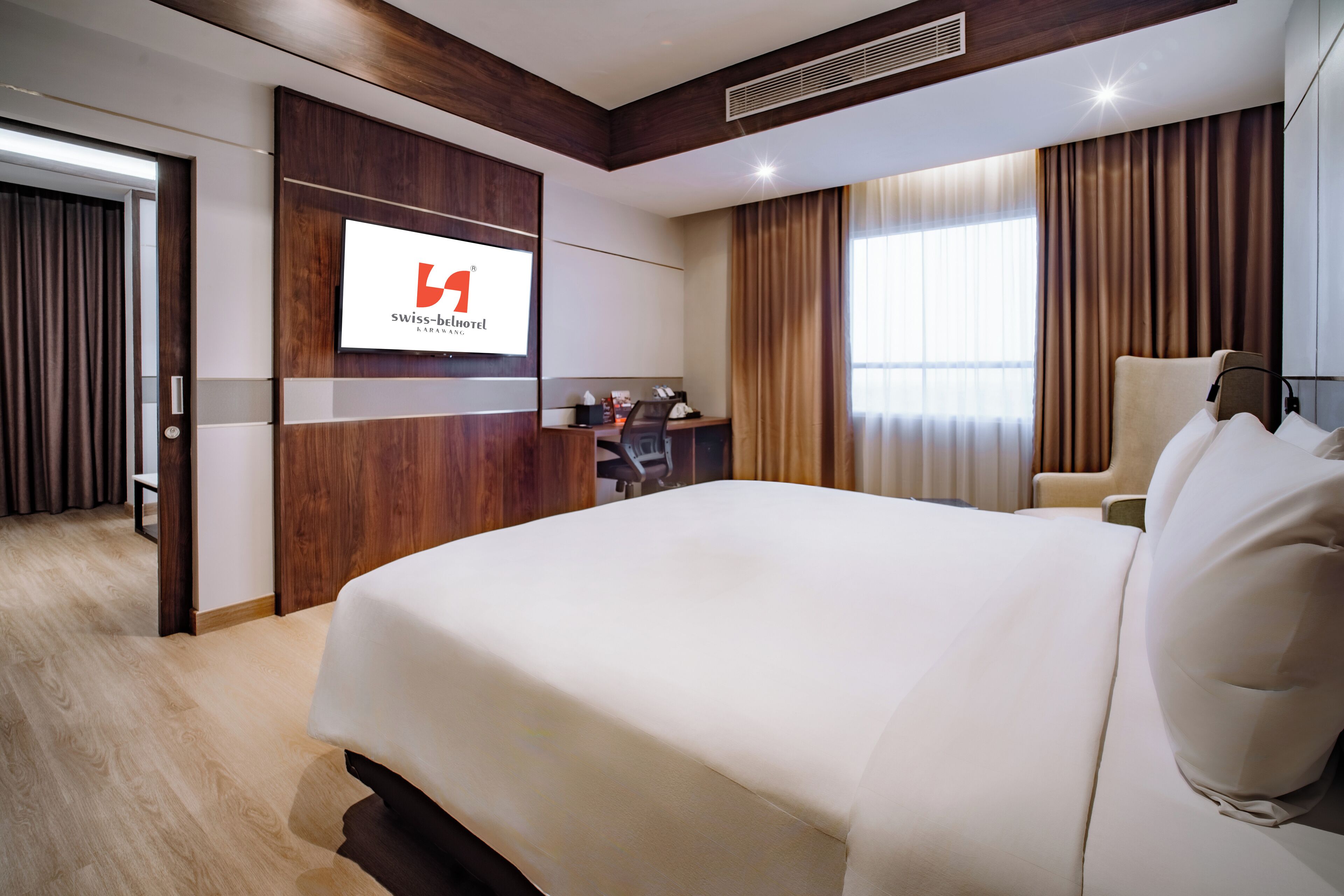 Een hotelkamer met een groot bed, een bureau met stoel, een televisiescherm en een kledingkast.