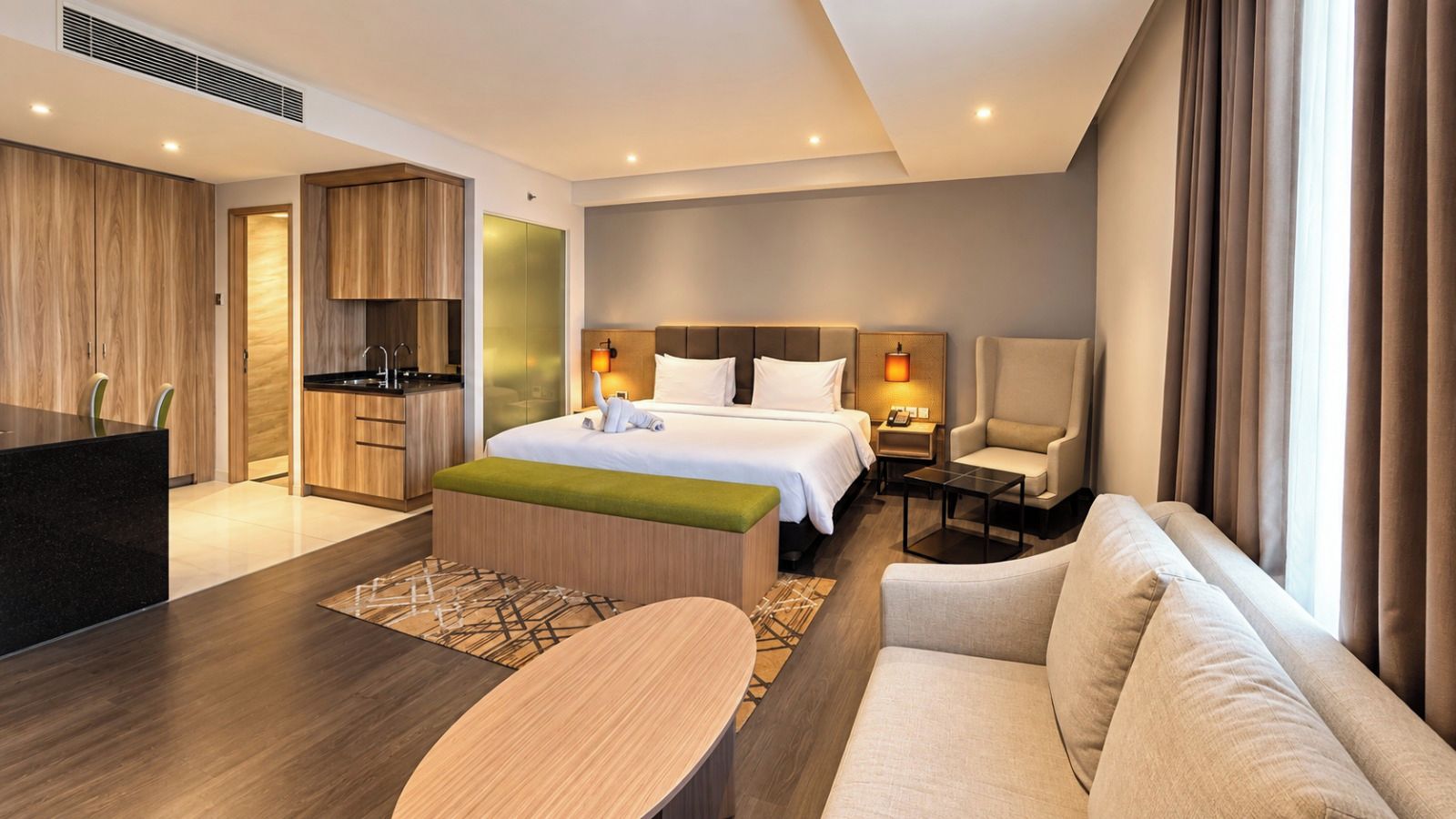 A hotel room with a bed, a sofa, a desk, a chair, and a kitchenette.
