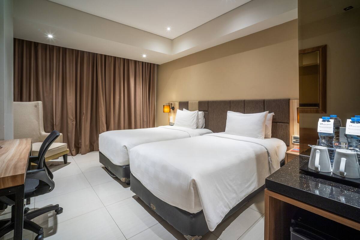 Habitación de hotel con dos camas, un escritorio, una silla, un espacio para café y un gran ventanal con cortinas.