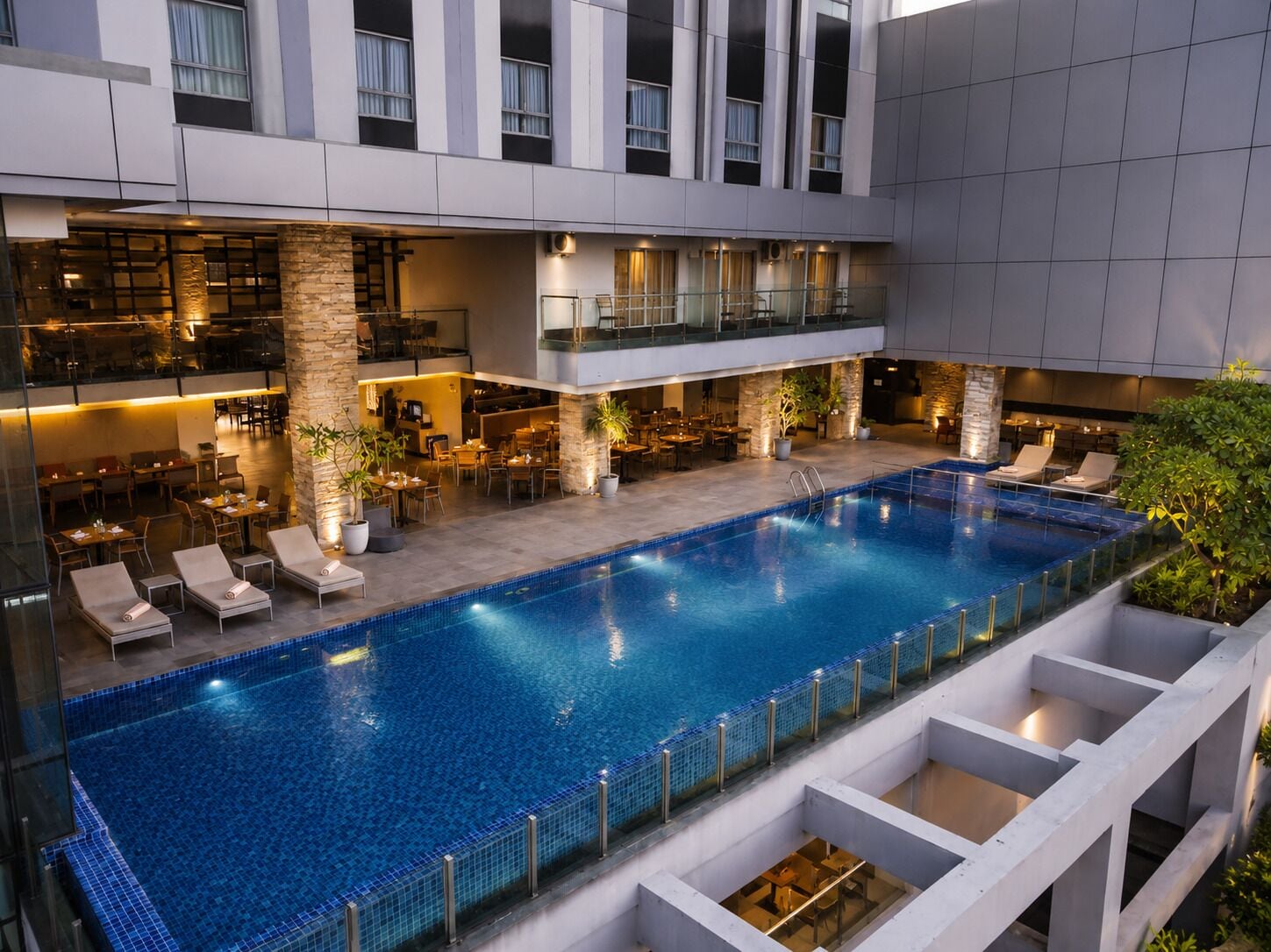 A modern indoor pool with lounge chairs, a dining area, and a bar.