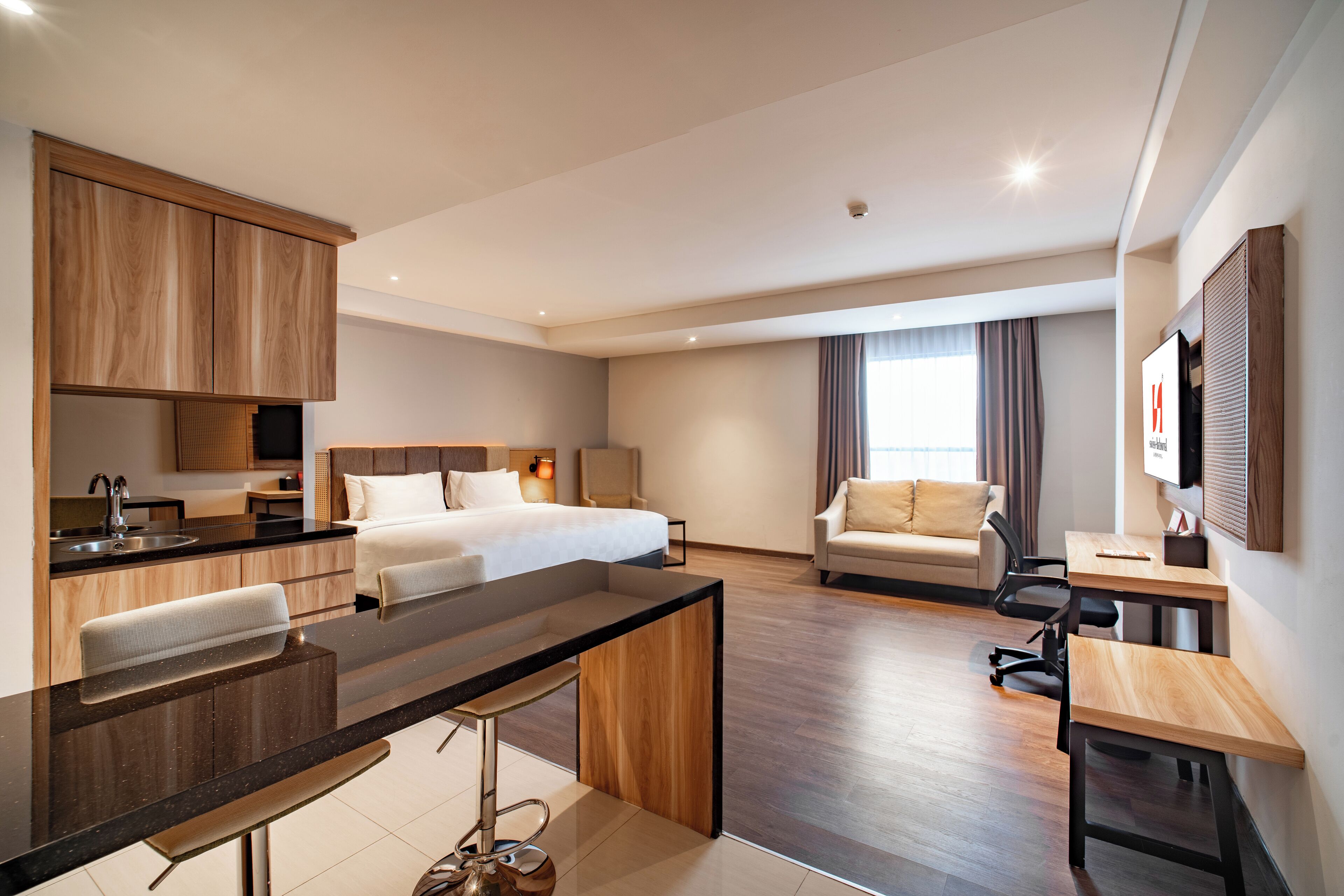 Una habitación de hotel moderna con kitchenette, una cama, un sofá, un escritorio y un televisor.