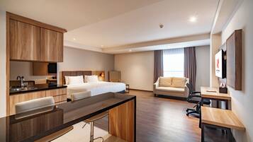 Una habitación de hotel moderna con kitchenette, una cama, un sofá, un escritorio y un televisor.