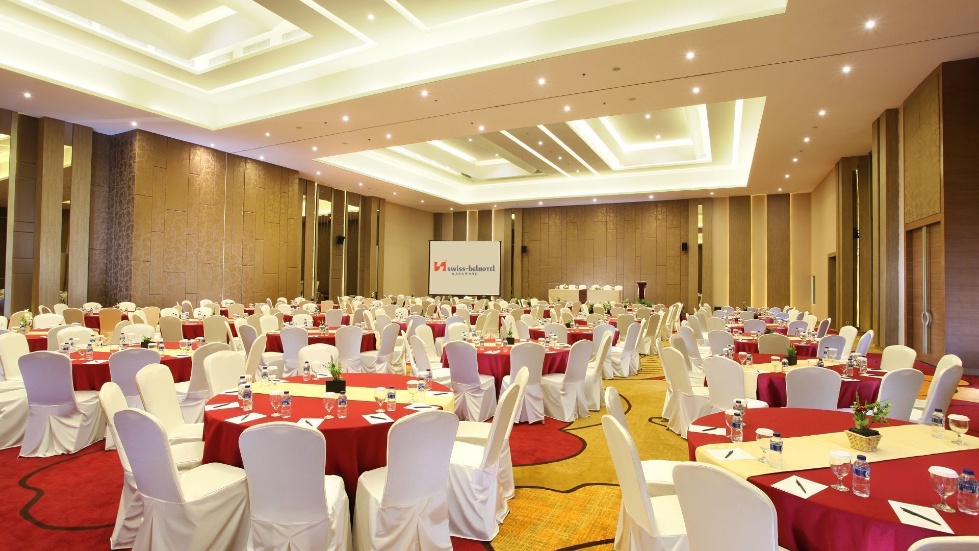 A large conference room with multiple tables, white chairs, and a presentation screen.