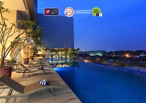 Zona de piscina con sillones reclinables y plantas en macetas, un edificio moderno al fondo e insignias de certificación que indican medidas de seguridad e higiene.