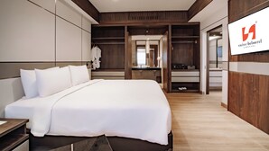 Een moderne hotelkamer met een groot bed, een inloopkast en een televisie waarop de naam van het hotel staat.