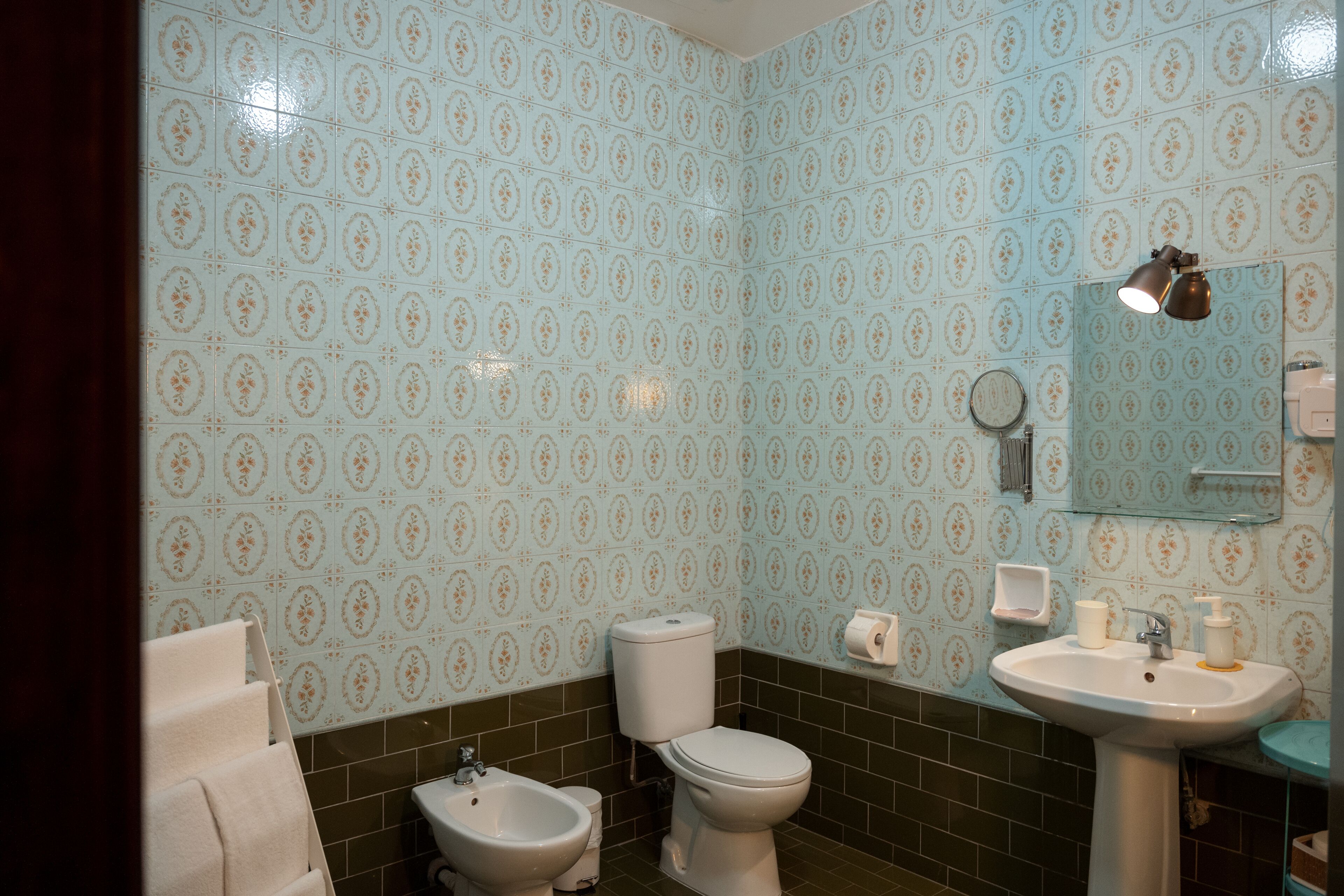 A bathroom with a toilet, bidet, and sink, all with matching patterned tiles.