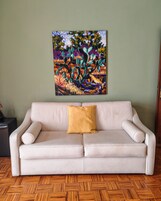 Un divano beige con un cuscino color senape, davanti a una parete verde, con un quadro astratto dai colori vivaci sopra.