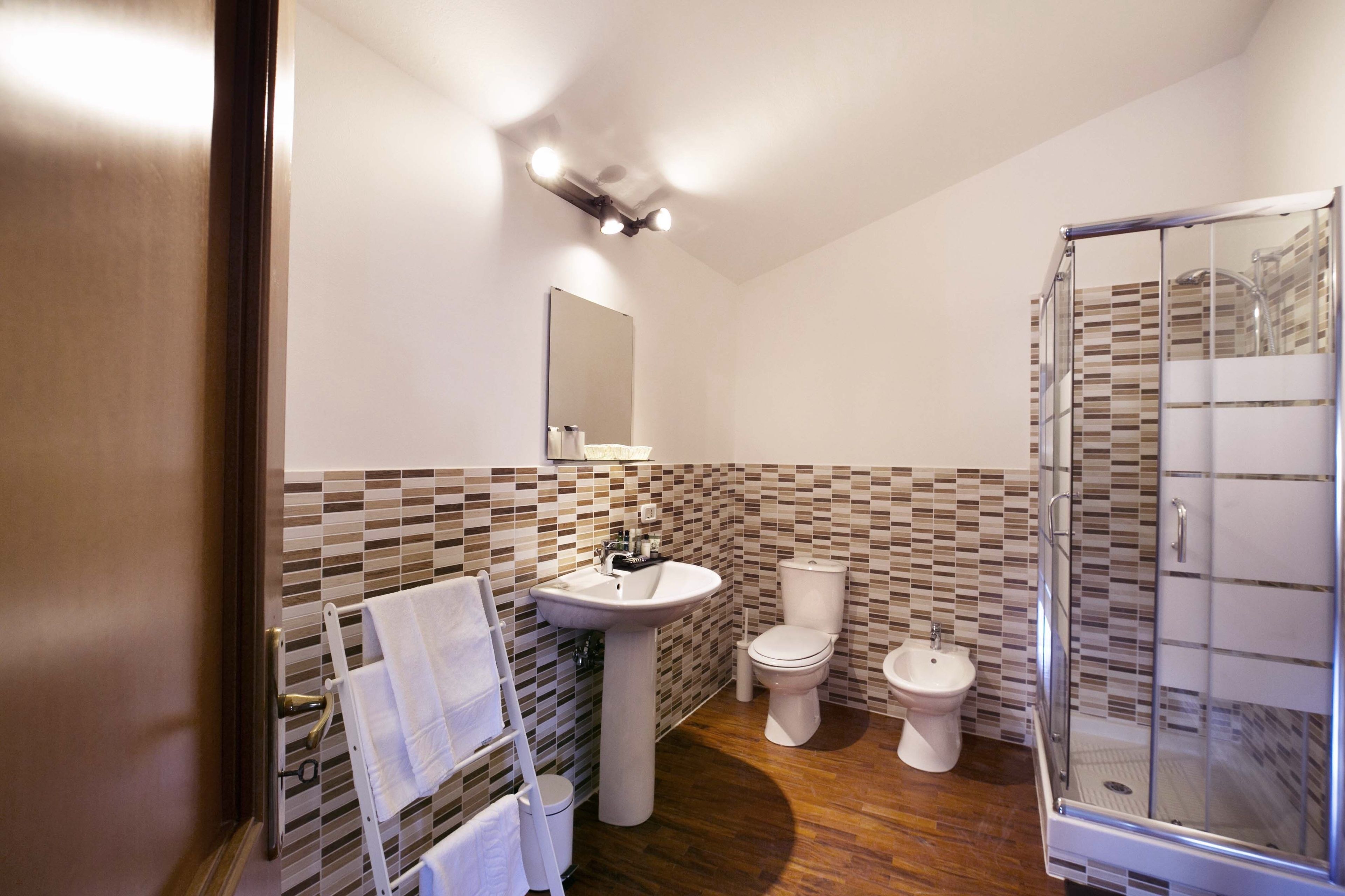 Uma casa de banho com painel de azulejos, pia, sanita, bidé e cabine de duche com portas de vidro.
