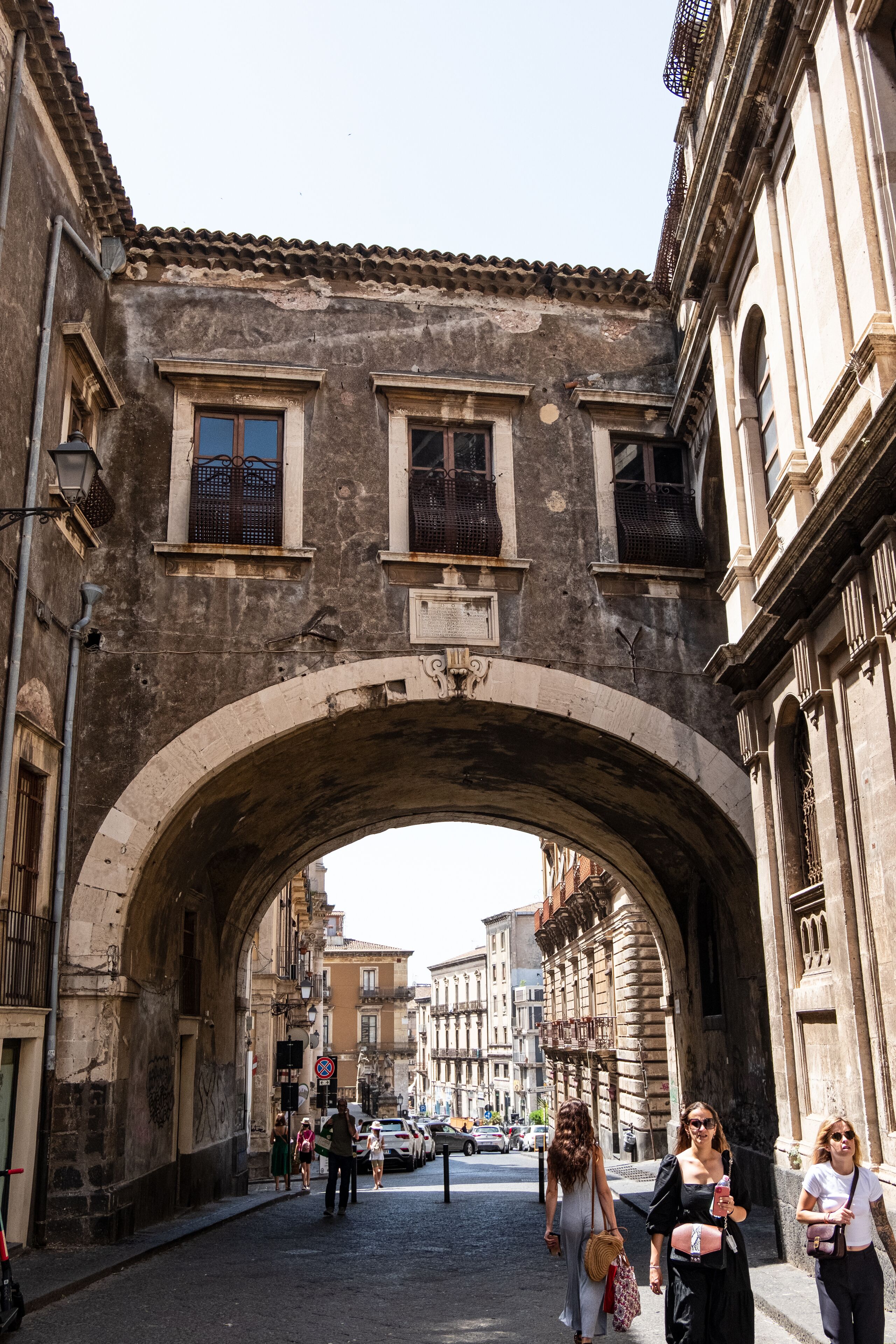 Uma ponte de pedra arqueada em um centro histórico da cidade, com pedestres passando por baixo.