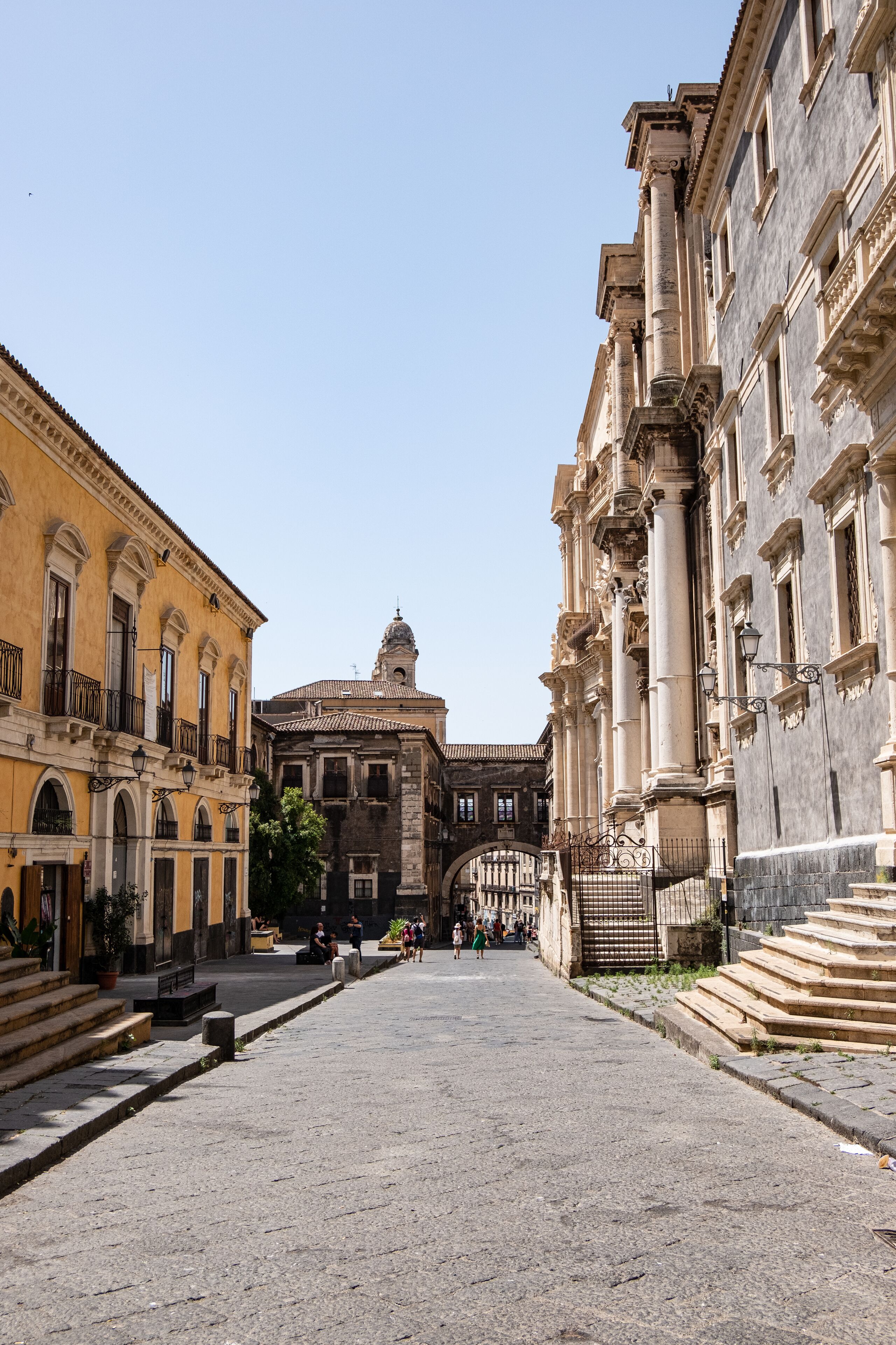 Una calle histórica con edificios de arquitectura clásica, un espacio abierto central y una torre de campanas al fondo.