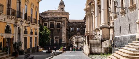 Una calle histórica con edificios de arquitectura clásica, un espacio abierto central y una torre de campanas al fondo.