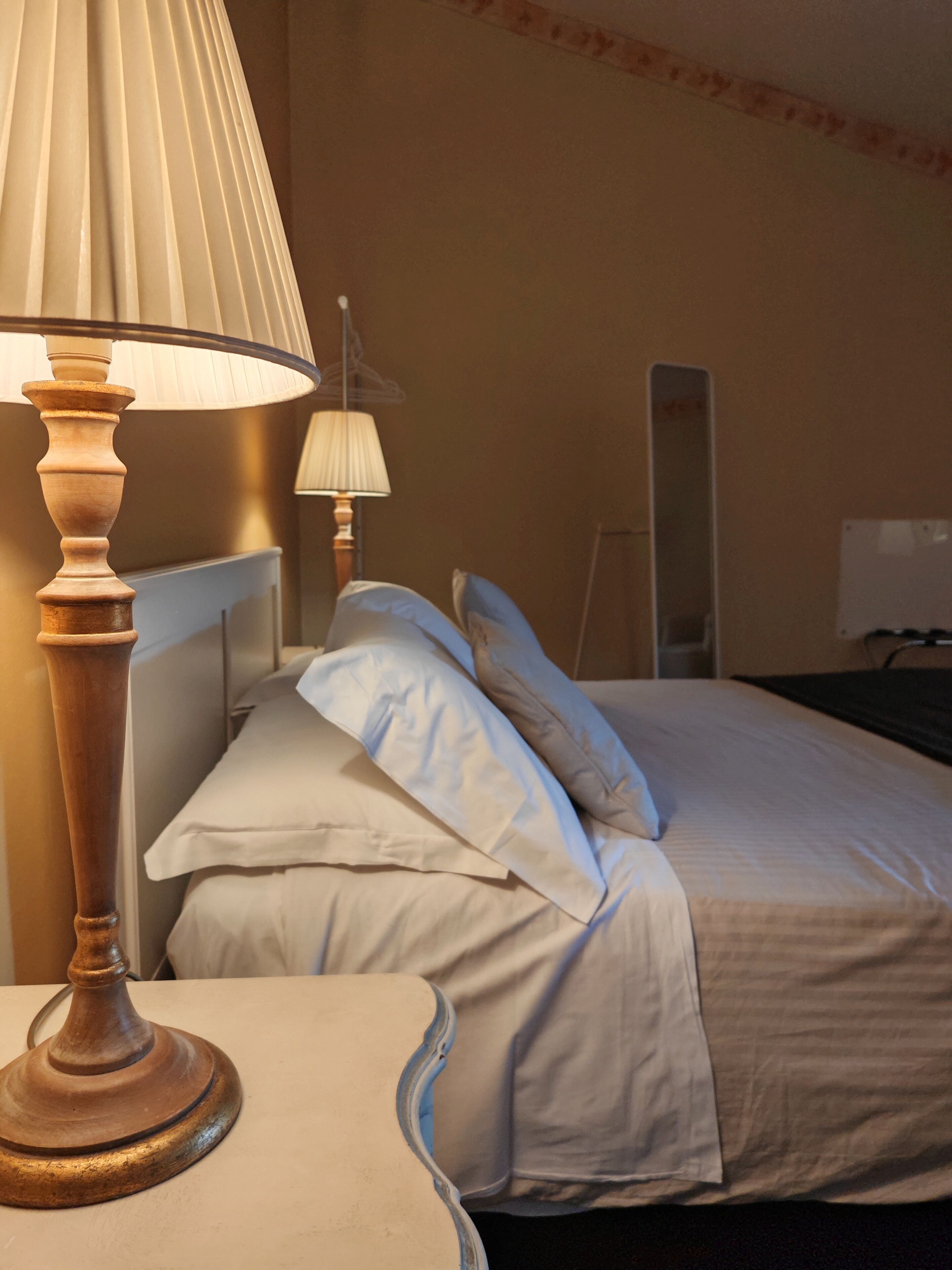 A hotel room with a bed, a bedside table with a lamp, and a mirror on the wall.