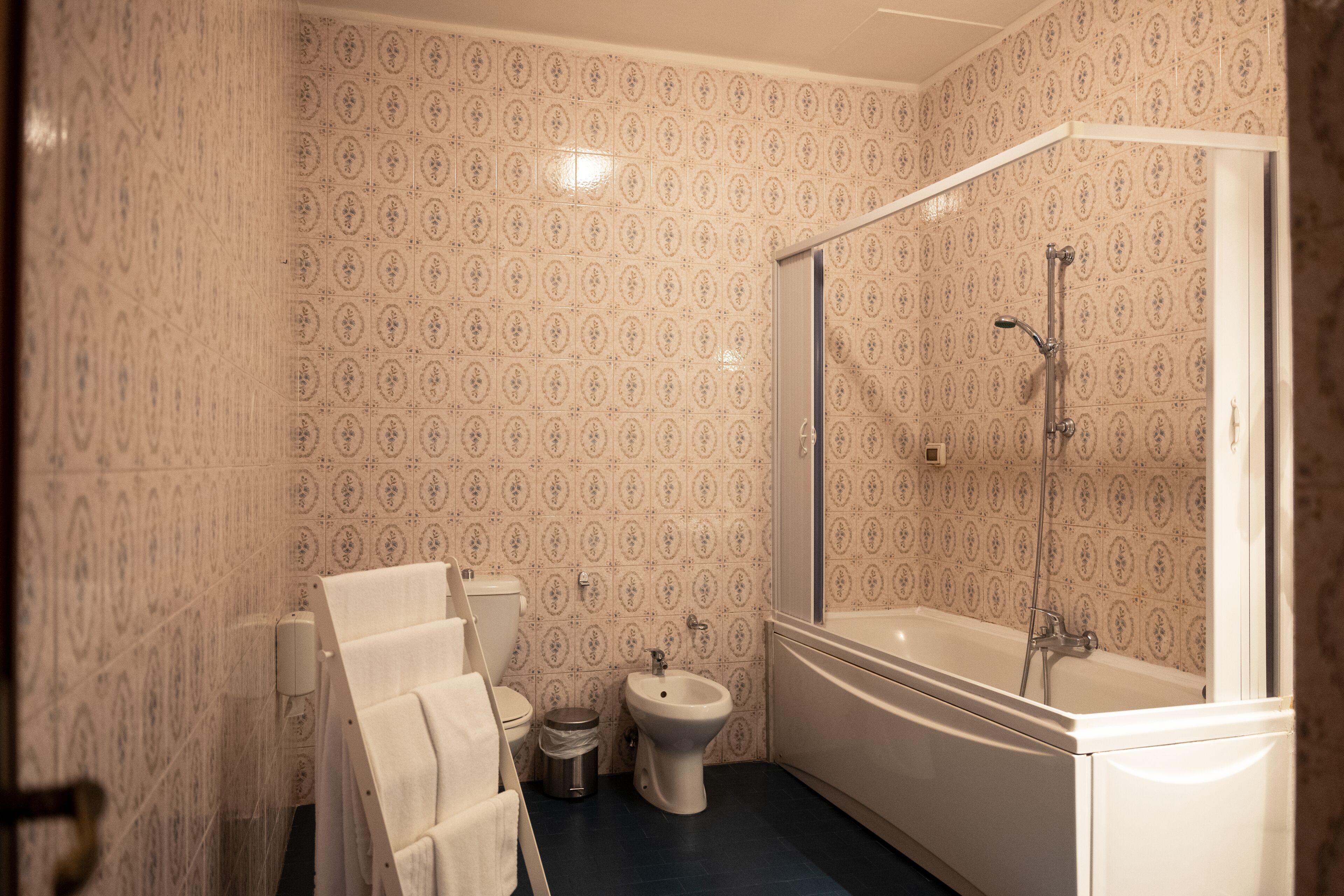 Une salle de bain avec un papier peint à motifs, des toilettes, un bidet, une baignoire et un porte-serviettes.
