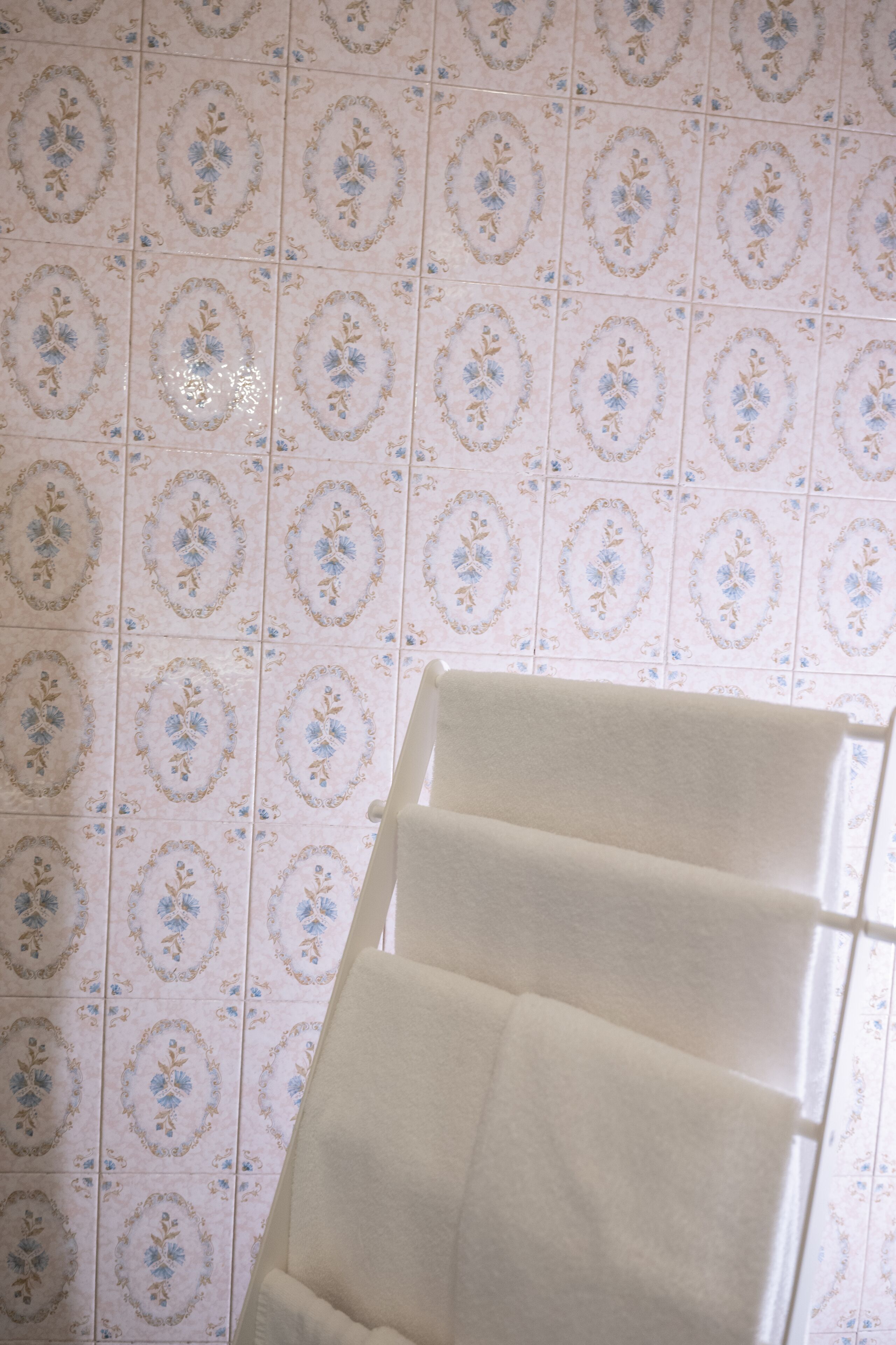 Un baño con un perchero blanco frente a una pared con un diseño de azulejos florales.