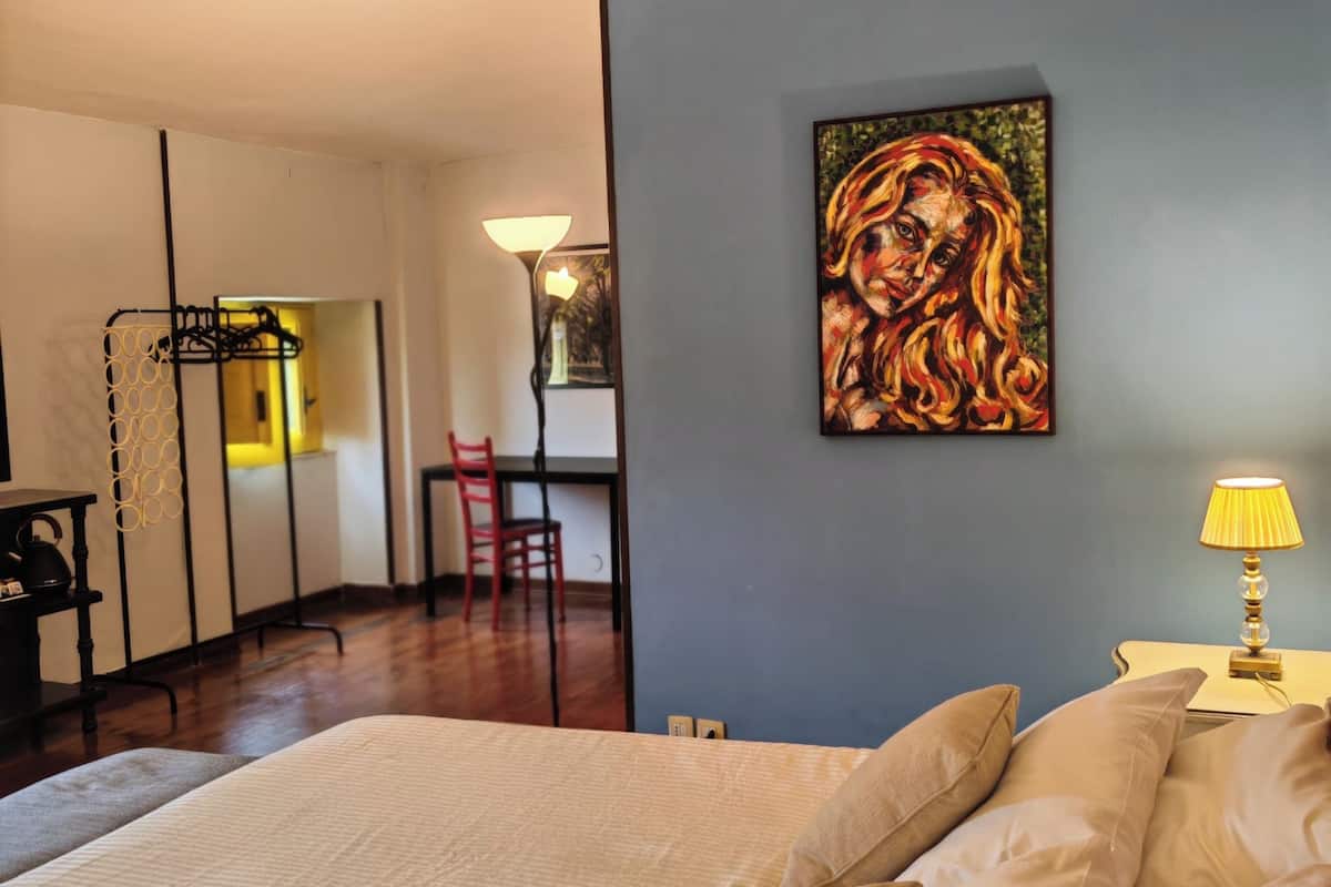 A bedroom with a large bed, a painting on the wall, and a desk with a chair.