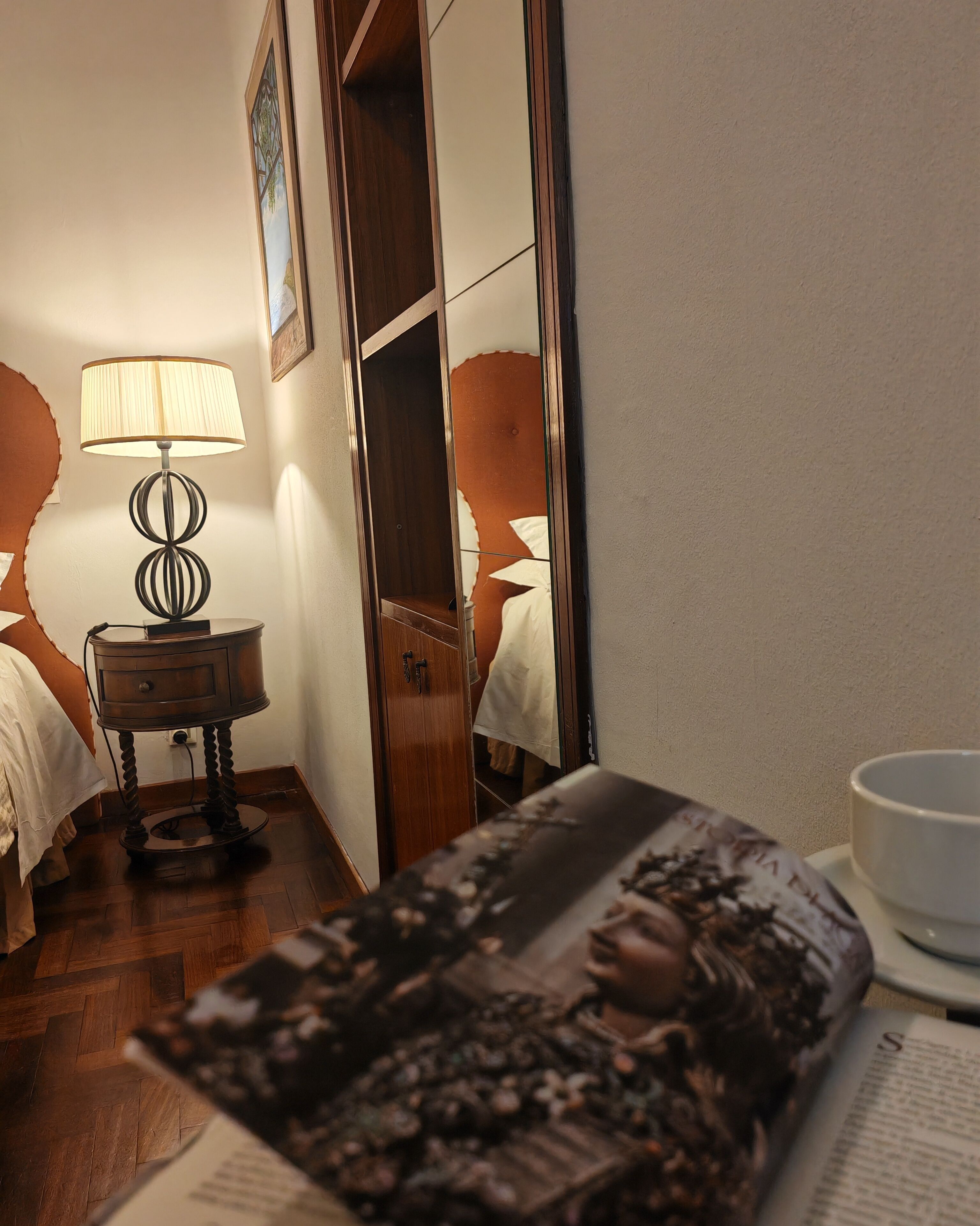 Ein Hotelzimmer mit Holzboden, einem Nachttisch mit Lampe, einem Spiegel und einem Bett mit weißer Bettdecke.