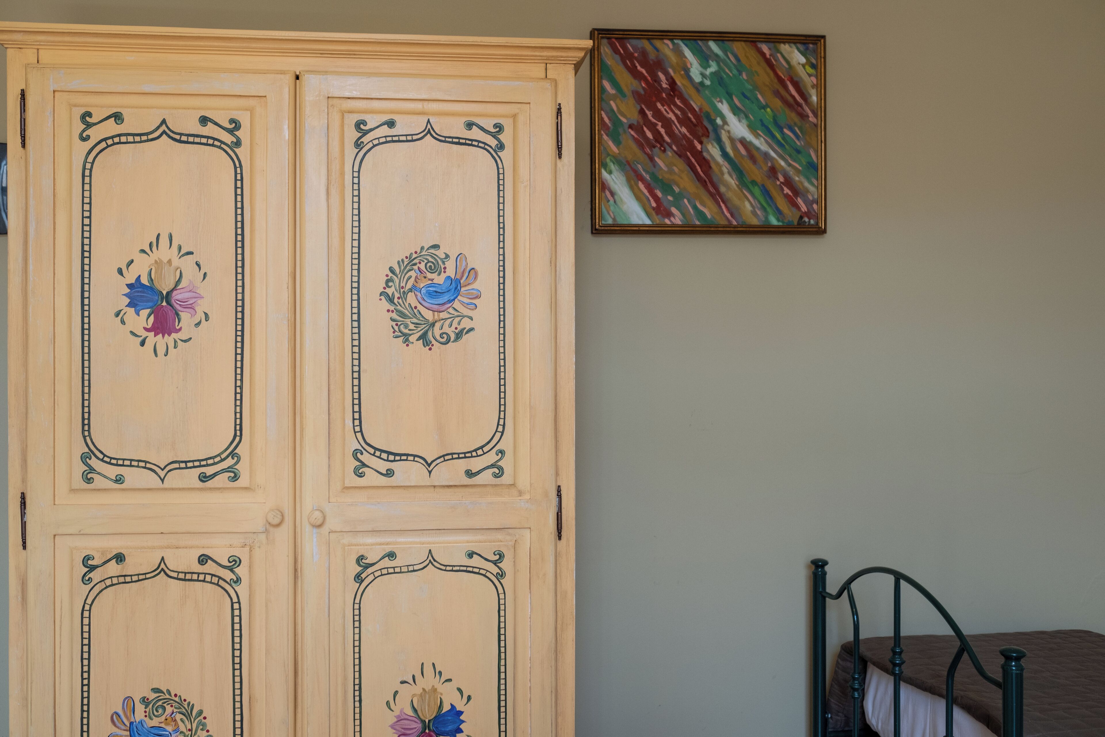 A bedroom with a bed, a wardrobe with floral designs, and a colorful abstract painting on the wall.