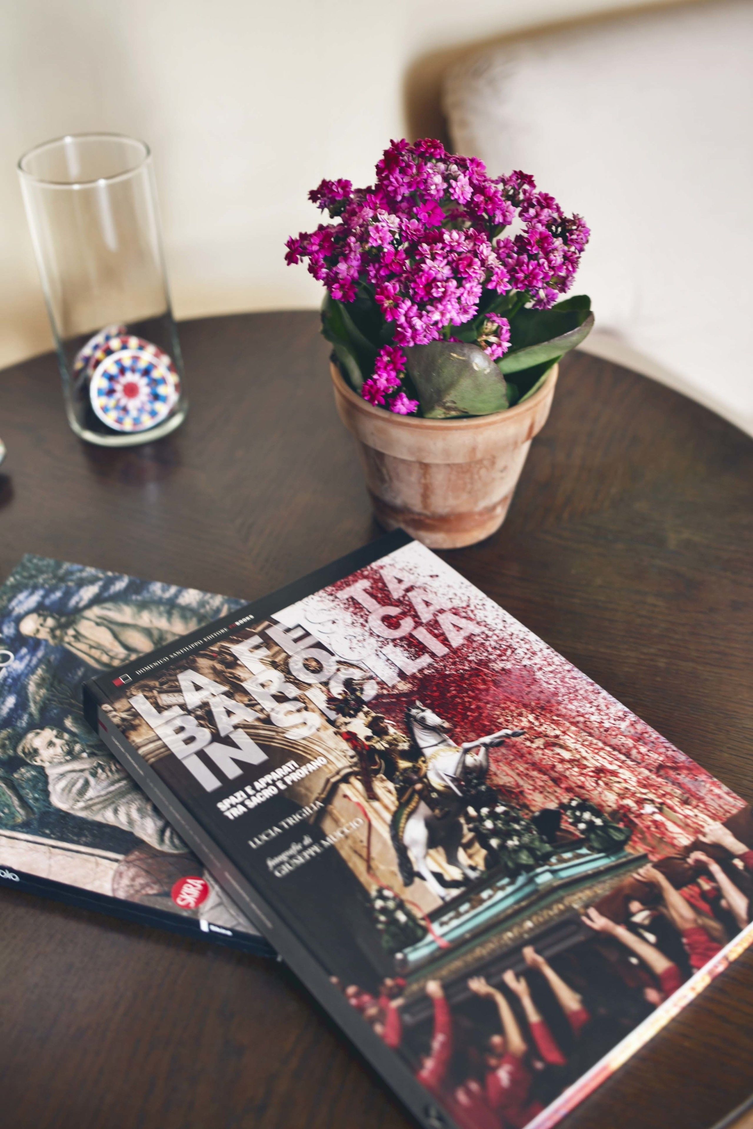 A table with a book titled "La Festa Barbi" and a potted plant with pink flowers.