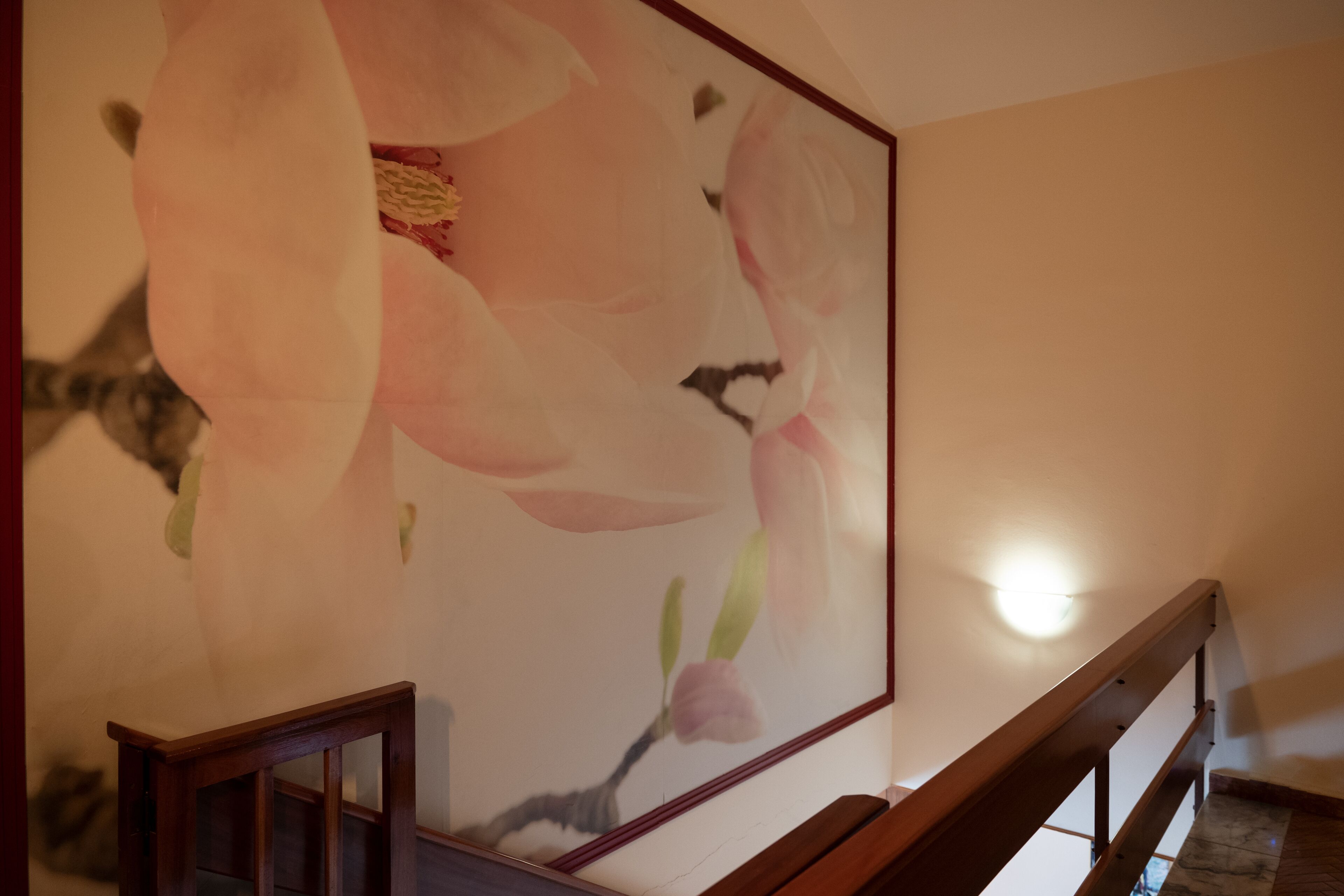 Una escalera con barandilla de madera y un cuadro de flores rosadas en la pared.