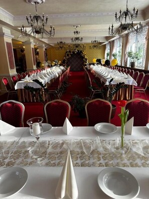 Un comedor formal con una larga mesa dispuesta para una comida, sillas tapizadas en rojo y un candelabro.