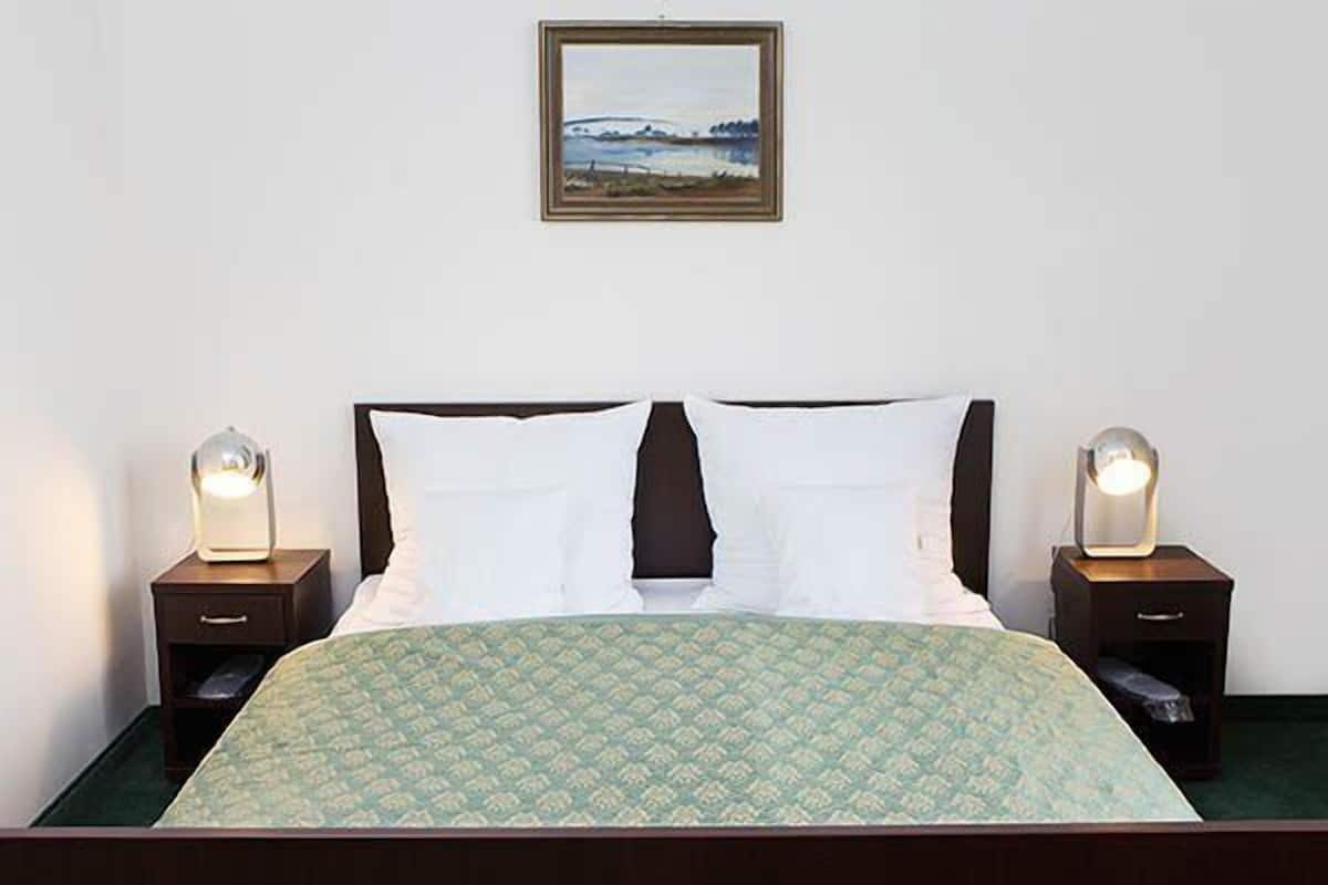 A neatly made bed with a patterned bedspread, two bedside lamps, and a framed picture on the wall.
