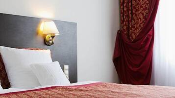 Una habitación de hotel con una cama, una mesita de noche, una lámpara y una ventana con cortinas.
