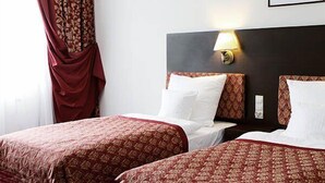 Habitación de hotel con dos camas, cada una con una colcha estampada, cabecero oscuro y una lámpara fijada a la pared.