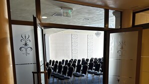 Un salón de conferencias con filas de sillas, una lámpara en el techo y una puerta con paneles decorativos.