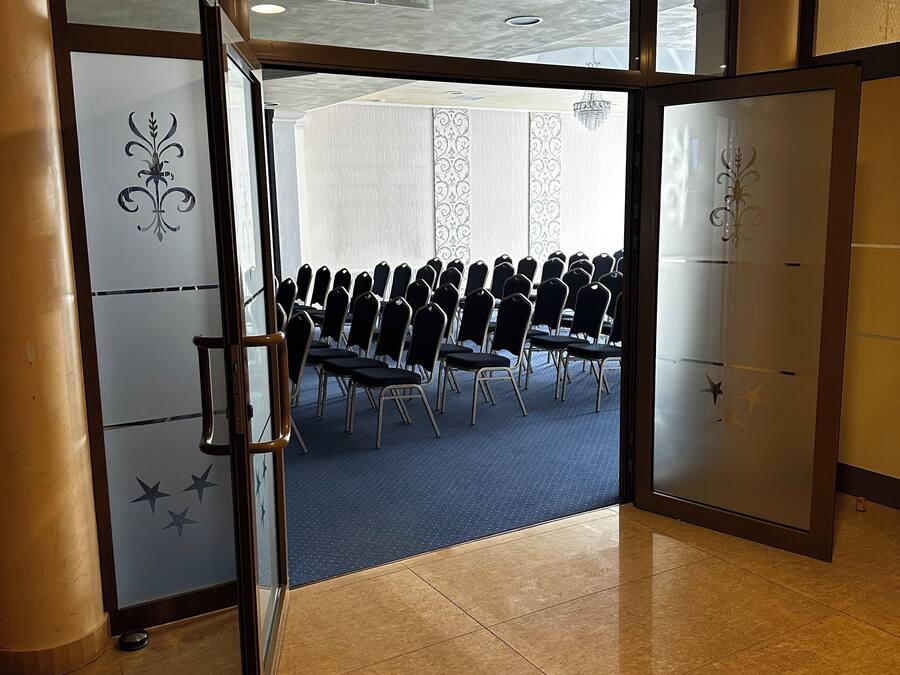 Ein Konferenzraum mit Reihen von Stühlen, einer Deckenleuchte und einer Tür mit dekorativen Verzierungen.