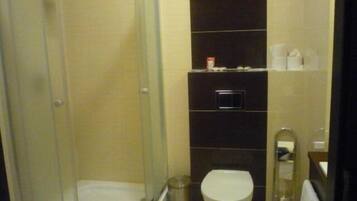 A bathroom with a glass-enclosed shower, a toilet, and a shelf with toiletries.