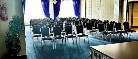 A conference room with rows of chairs, a table, and a large window with blue curtains.