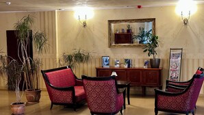 Un vestíbulo con sillas de color rojo con estampado, un mostrador de recepción de madera y plantas en macetas.