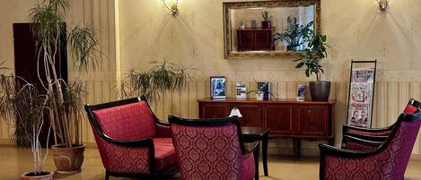 A lobby with red patterned chairs, a wooden reception desk, and potted plants.